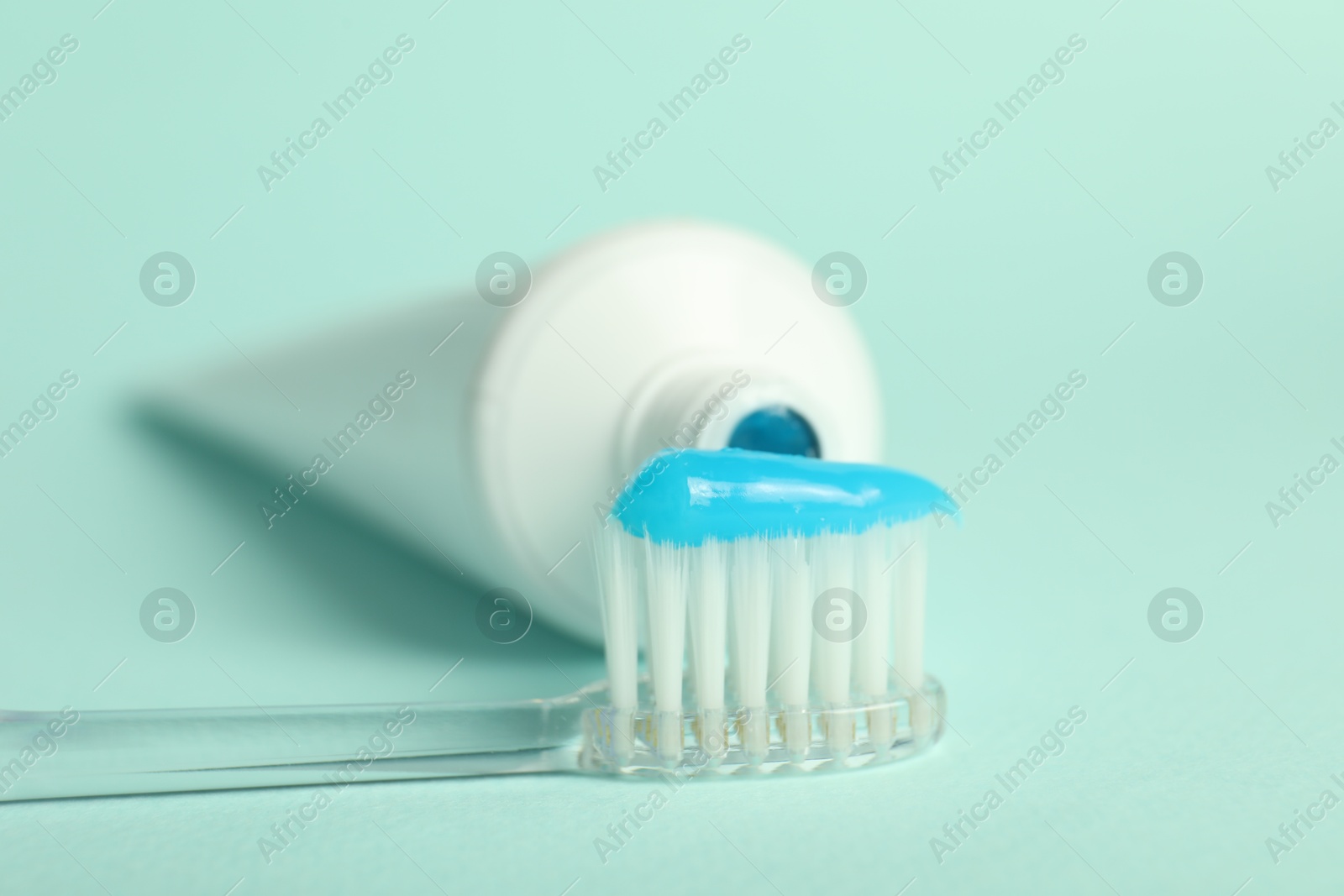 Photo of Toothbrush with toothpaste and tube on light blue background, closeup