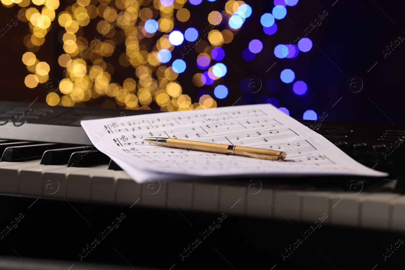 Photo of Sheets with notes and pen on piano against blurred lights, closeup. Bokeh effect