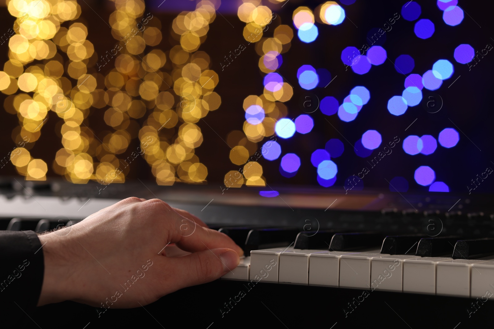 Photo of Man playing piano against blurred lights, closeup. Bokeh effect