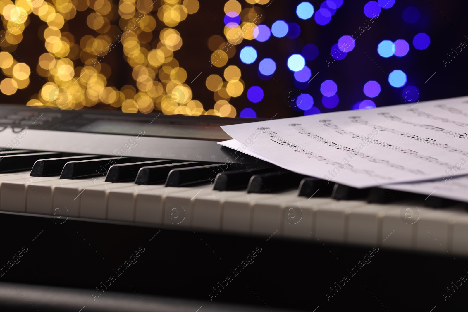 Photo of Sheets with notes on piano against blurred lights, closeup. Bokeh effect