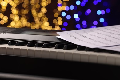 Photo of Sheets with notes on piano against blurred lights, closeup. Bokeh effect