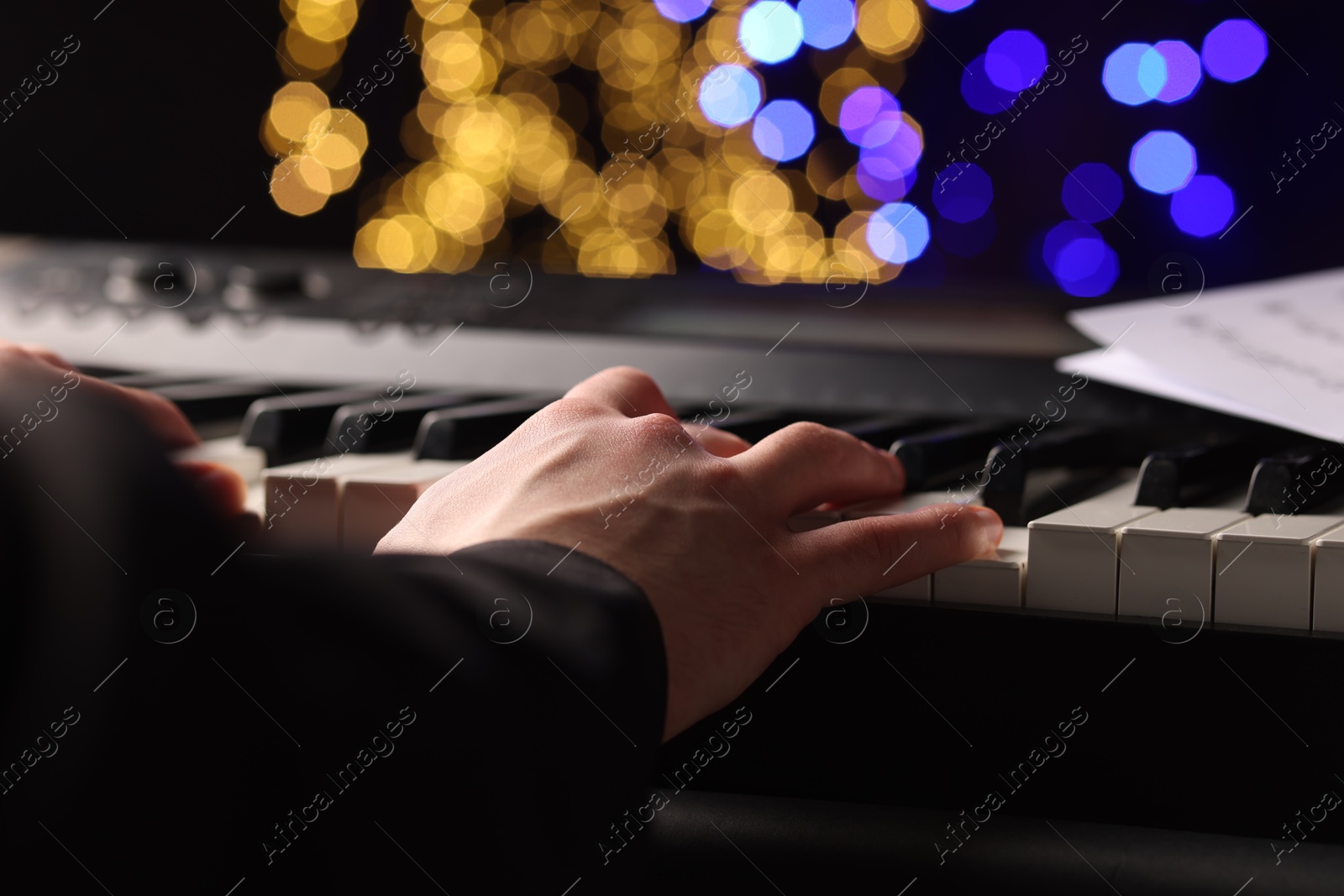 Photo of Man playing piano against blurred lights, closeup. Bokeh effect