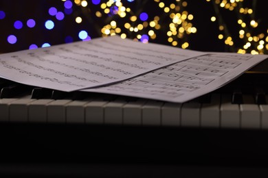 Photo of Sheets with notes on piano against blurred lights, closeup. Bokeh effect