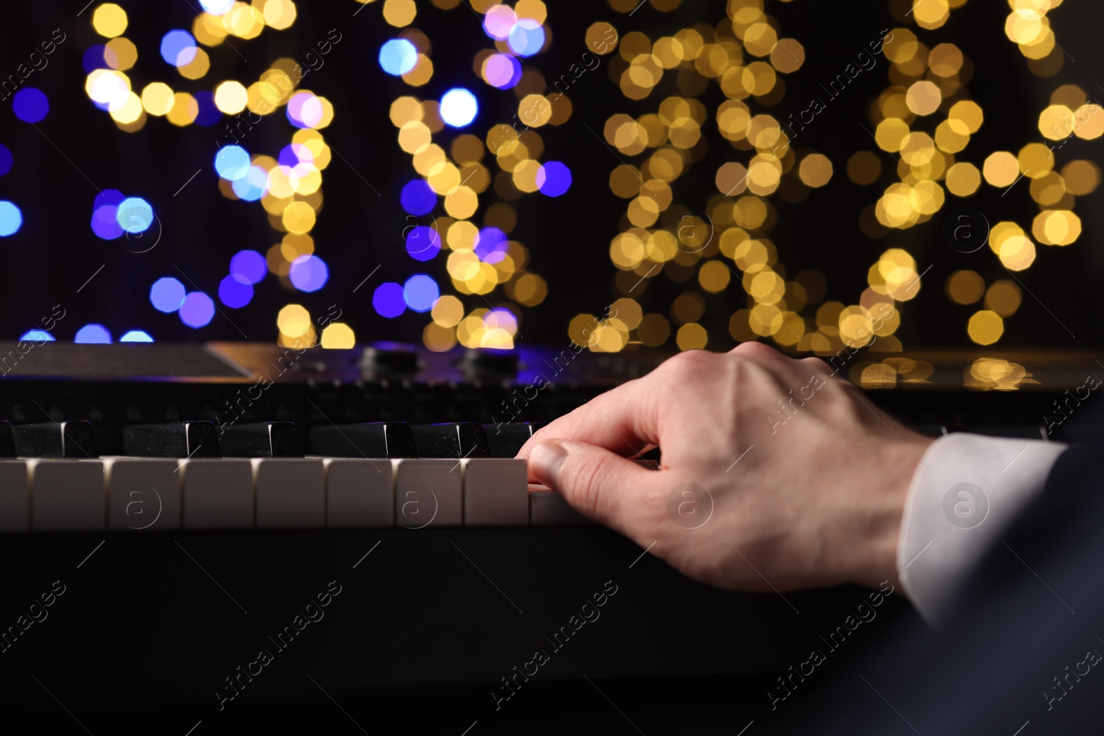 Photo of Man playing piano against blurred lights, closeup. Bokeh effect