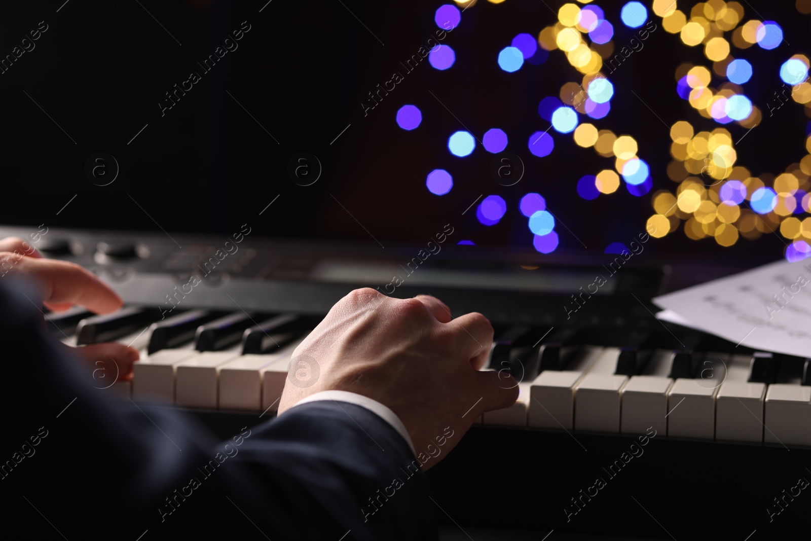 Photo of Man playing piano against blurred lights, closeup. Bokeh effect