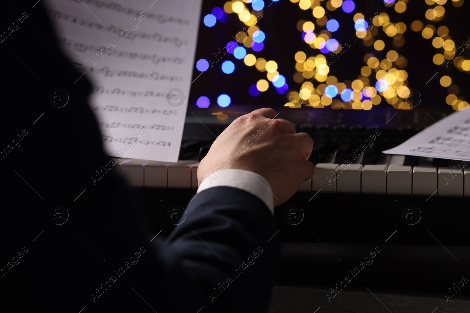 Photo of Man playing piano against blurred lights, closeup. Bokeh effect