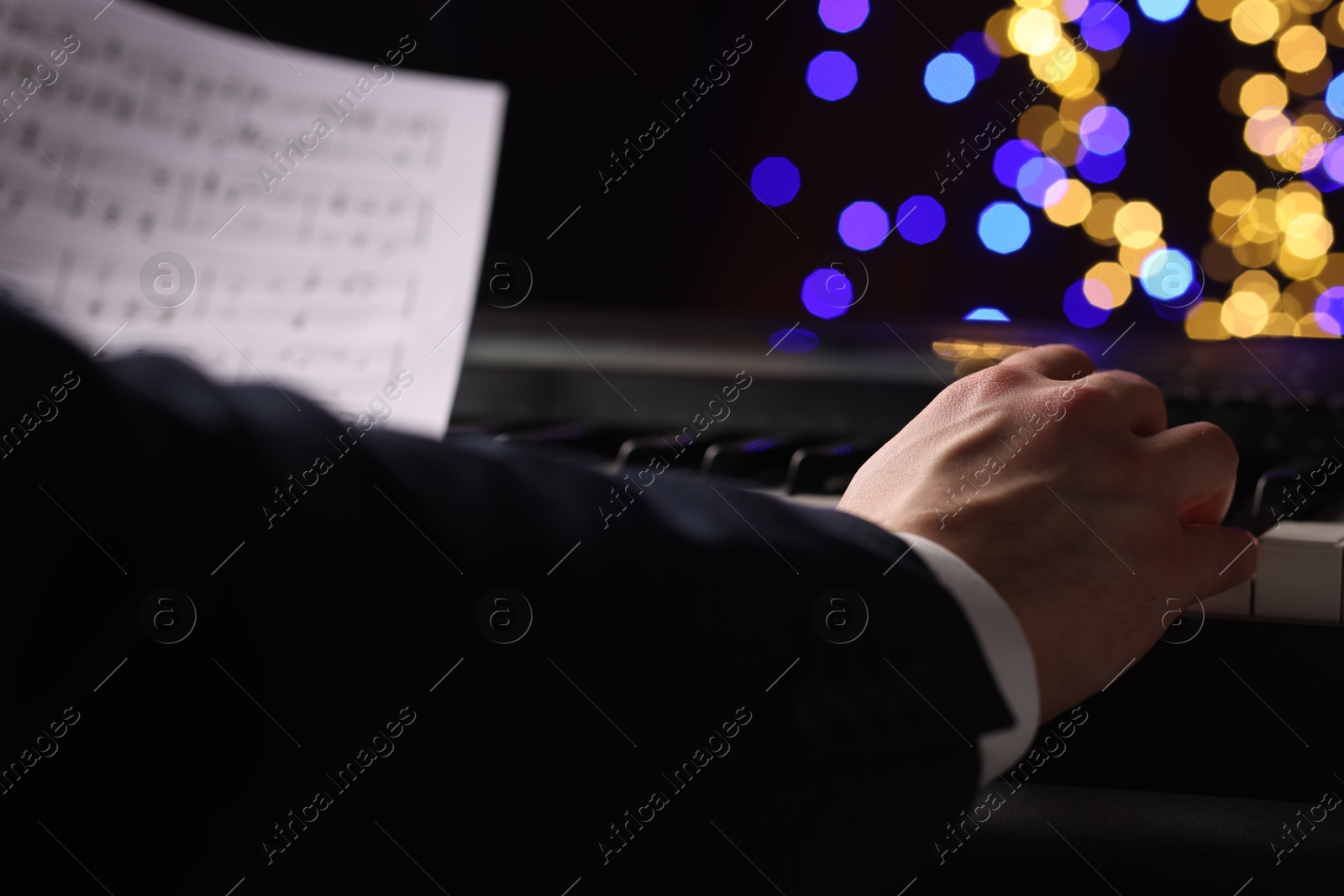 Photo of Man playing piano against blurred lights, closeup. Bokeh effect