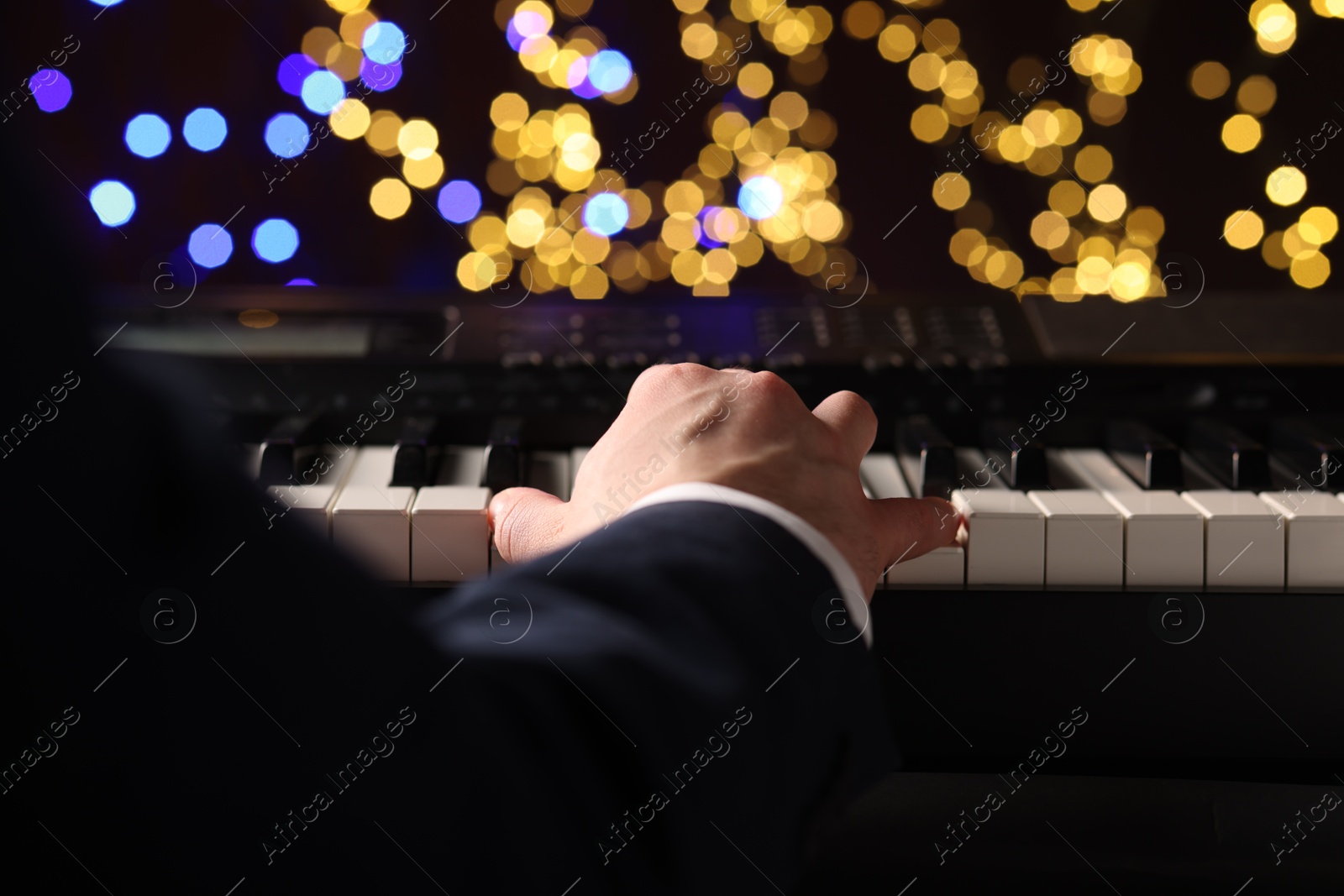 Photo of Man playing piano against blurred lights, closeup. Bokeh effect