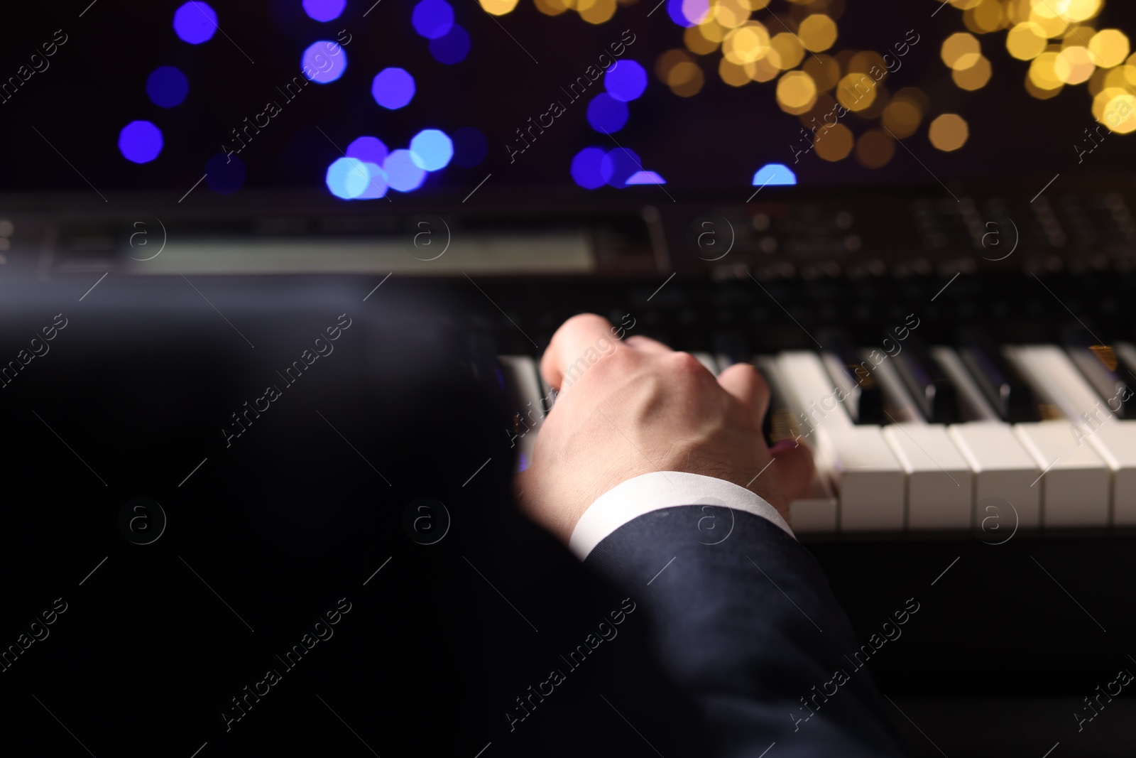 Photo of Man playing piano against blurred lights, closeup. Bokeh effect