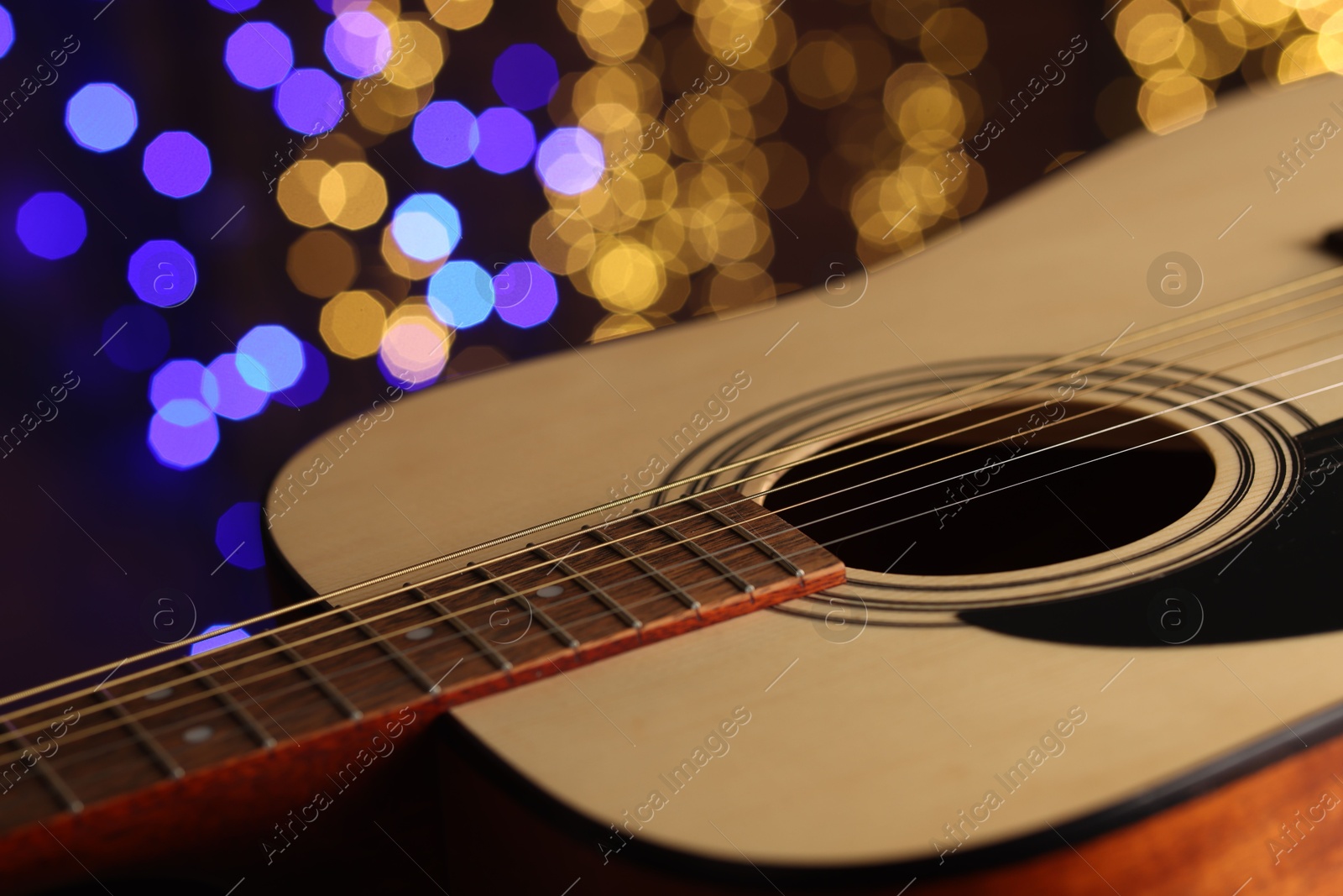 Photo of Guitar against blurred lights, closeup. Bokeh effect