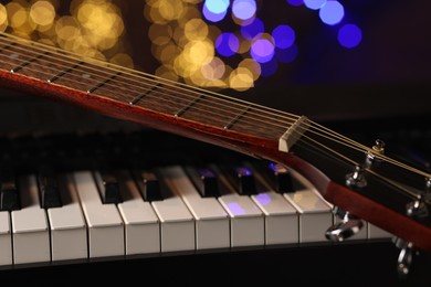 Photo of Guitar on piano against blurred lights, closeup. Bokeh effect