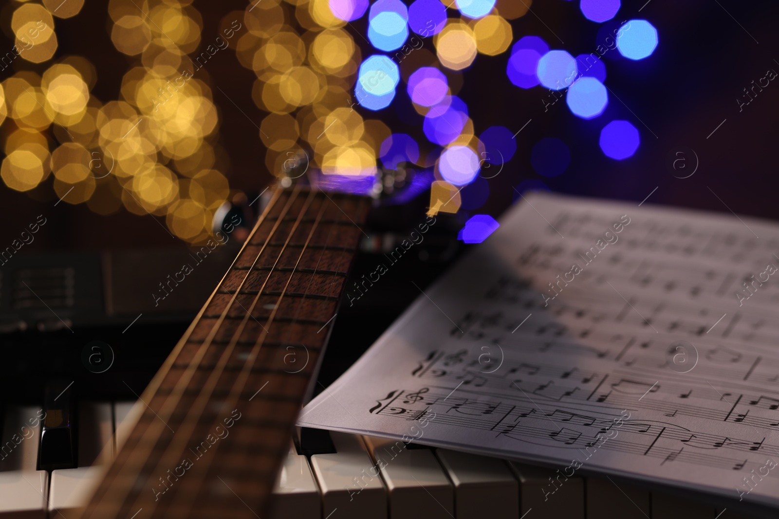 Photo of Guitar and notes on piano against blurred lights, closeup. Bokeh effect