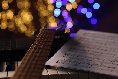 Photo of Guitar and notes on piano against blurred lights, closeup. Bokeh effect