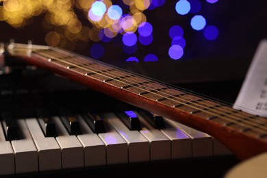 Photo of Guitar on piano against blurred lights, closeup. Bokeh effect