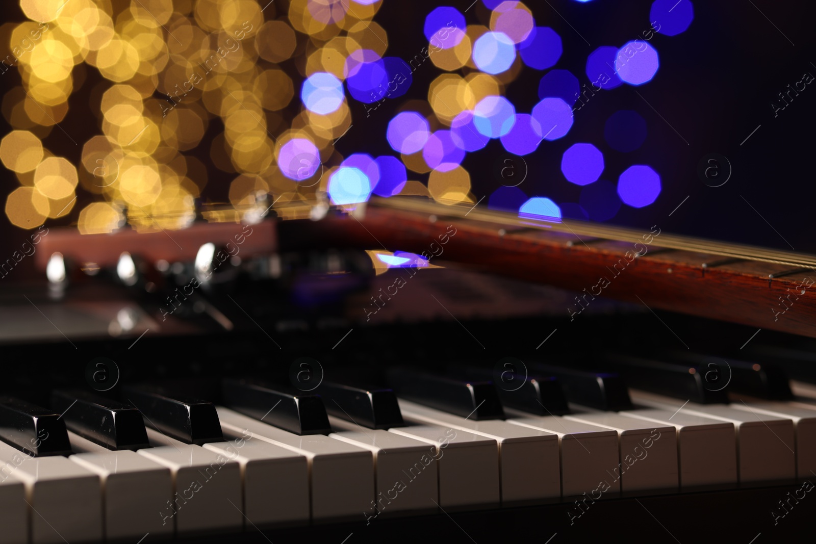 Photo of Guitar on piano against blurred lights, closeup. Bokeh effect