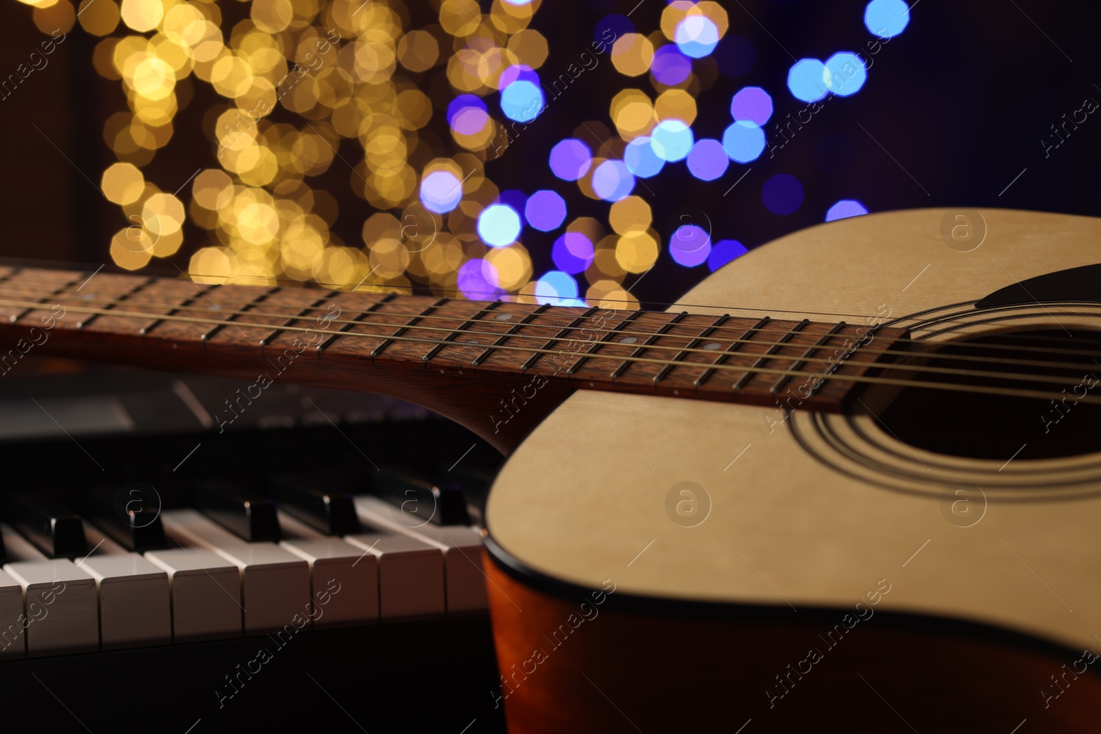 Photo of Guitar on piano against blurred lights, closeup. Bokeh effect