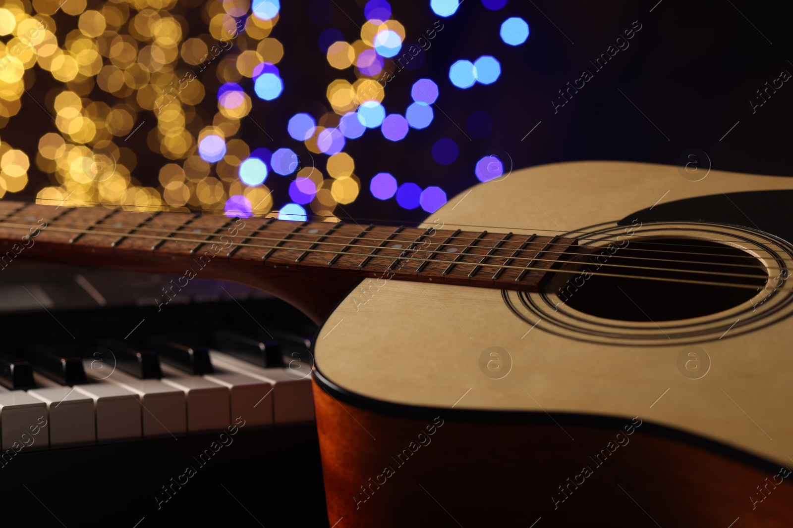 Photo of Guitar on piano against blurred lights, closeup. Bokeh effect