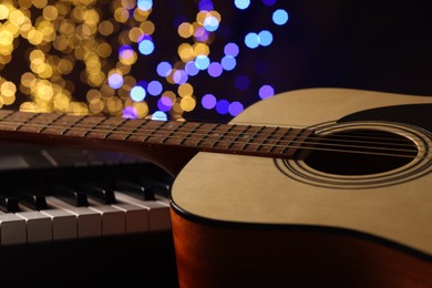 Photo of Guitar on piano against blurred lights, closeup. Bokeh effect