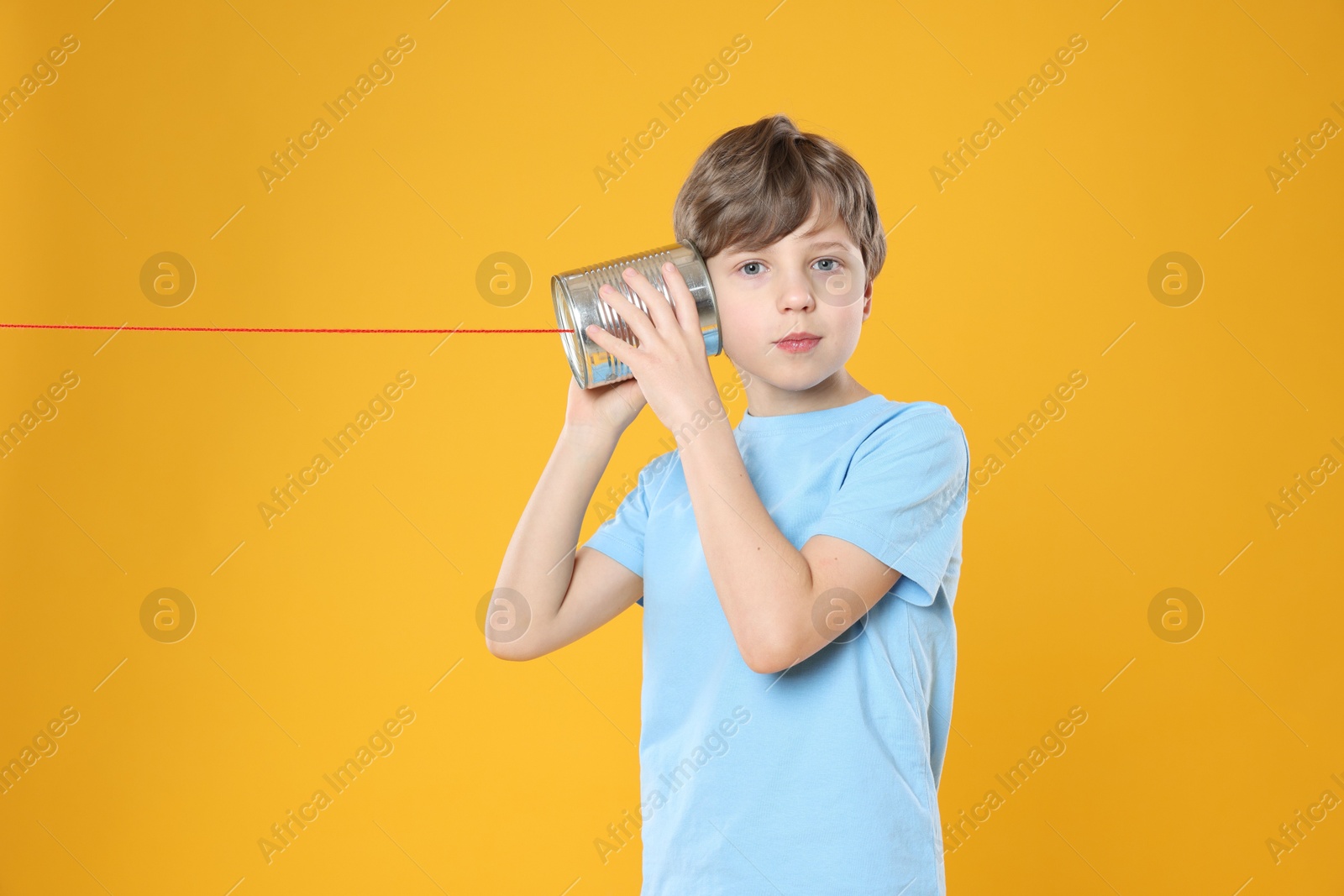 Photo of Boy using tin can telephone on orange background