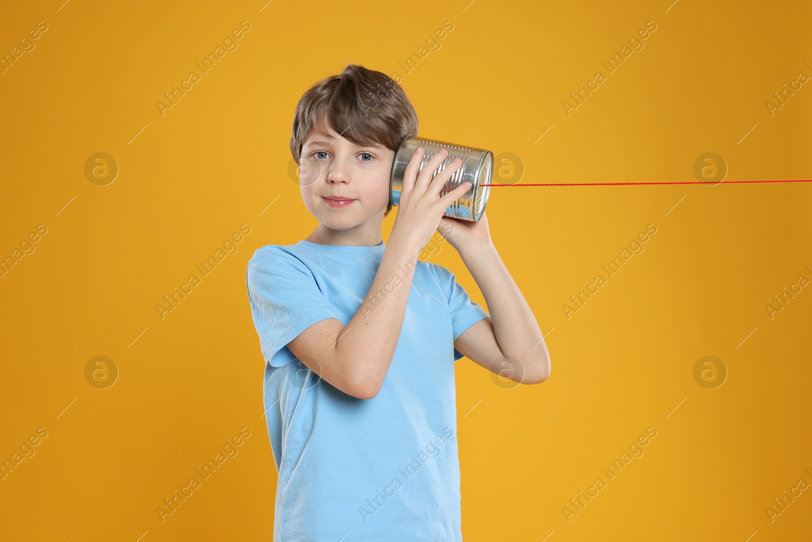 Photo of Boy using tin can telephone on orange background