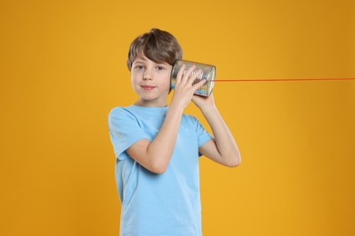 Photo of Boy using tin can telephone on orange background