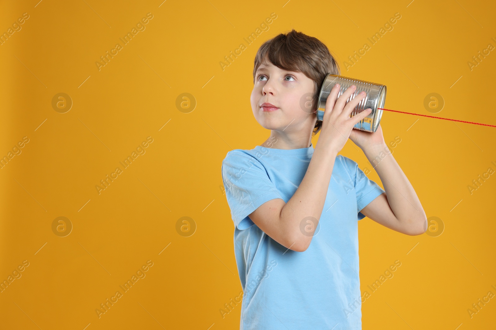 Photo of Boy using tin can telephone on orange background. Space for text