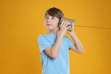 Photo of Boy using tin can telephone on orange background