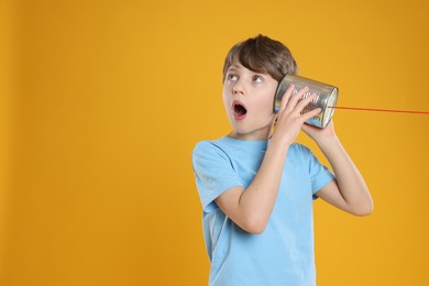 Photo of Surprised boy using tin can telephone on orange background. Space for text