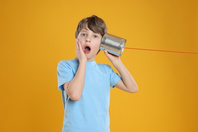 Photo of Surprised boy using tin can telephone on orange background