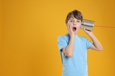 Photo of Surprised boy using tin can telephone on orange background. Space for text