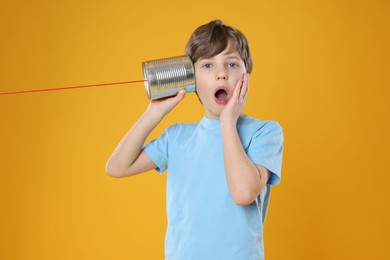 Photo of Surprised boy using tin can telephone on orange background