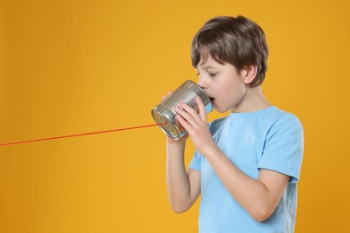 Photo of Boy using tin can telephone on orange background