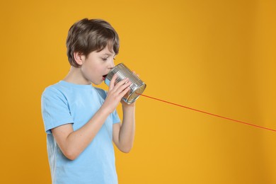 Photo of Boy using tin can telephone on orange background