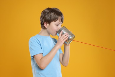 Photo of Boy using tin can telephone on orange background