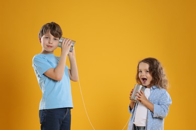 Boy and girl talking on tin can telephone against orange background