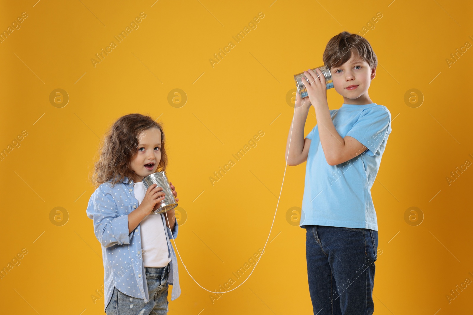 Photo of Boy and girl talking on tin can telephone against orange background