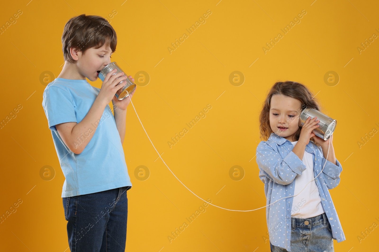 Photo of Boy and girl talking on tin can telephone against orange background