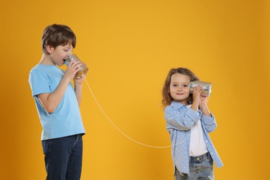 Photo of Boy and girl talking on tin can telephone against orange background