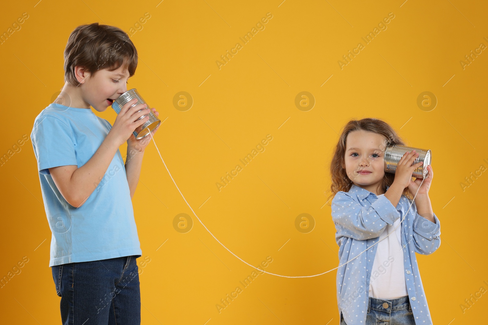 Photo of Boy and girl talking on tin can telephone against orange background