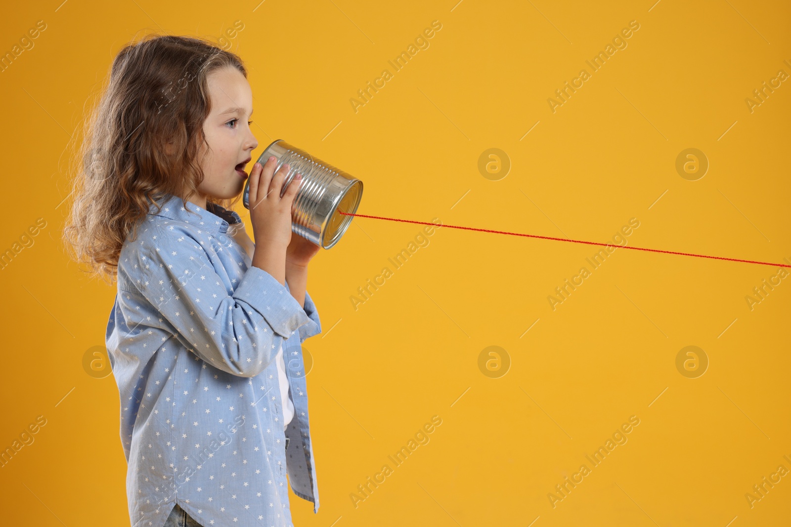 Photo of Girl using tin can telephone on orange background