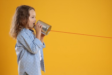 Photo of Girl using tin can telephone on orange background