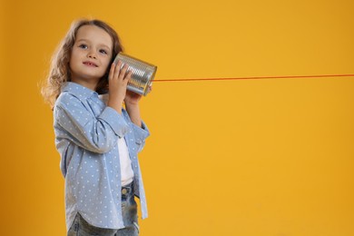 Photo of Girl using tin can telephone on orange background