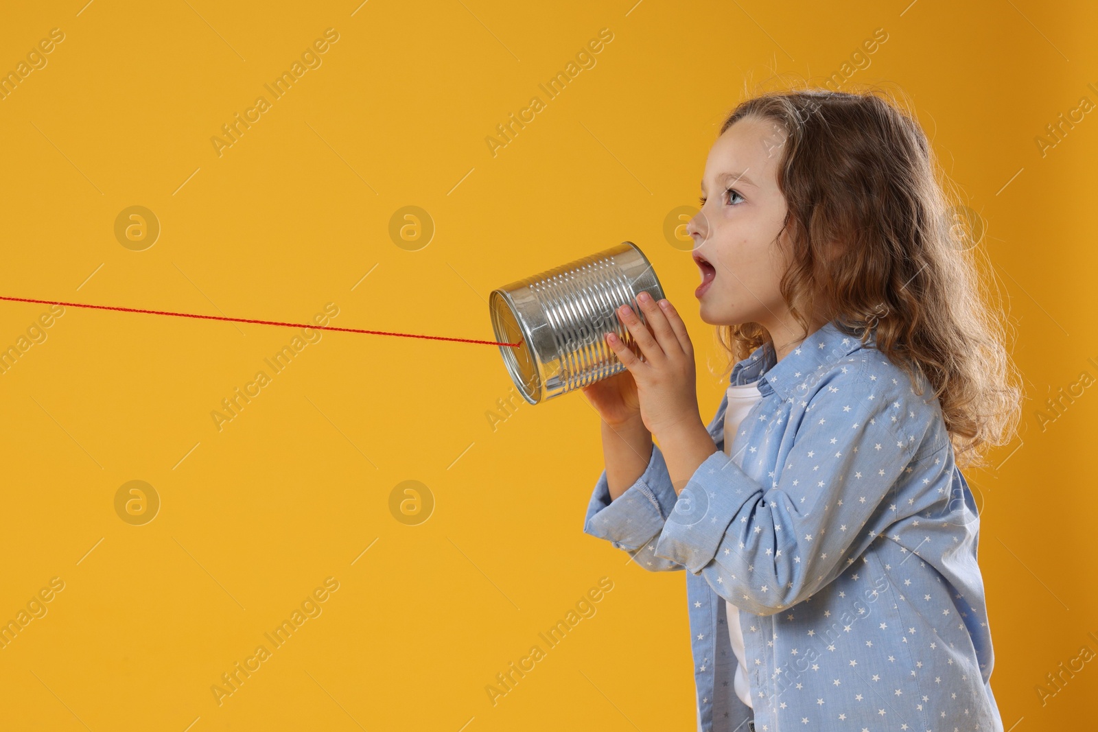 Photo of Girl using tin can telephone on orange background