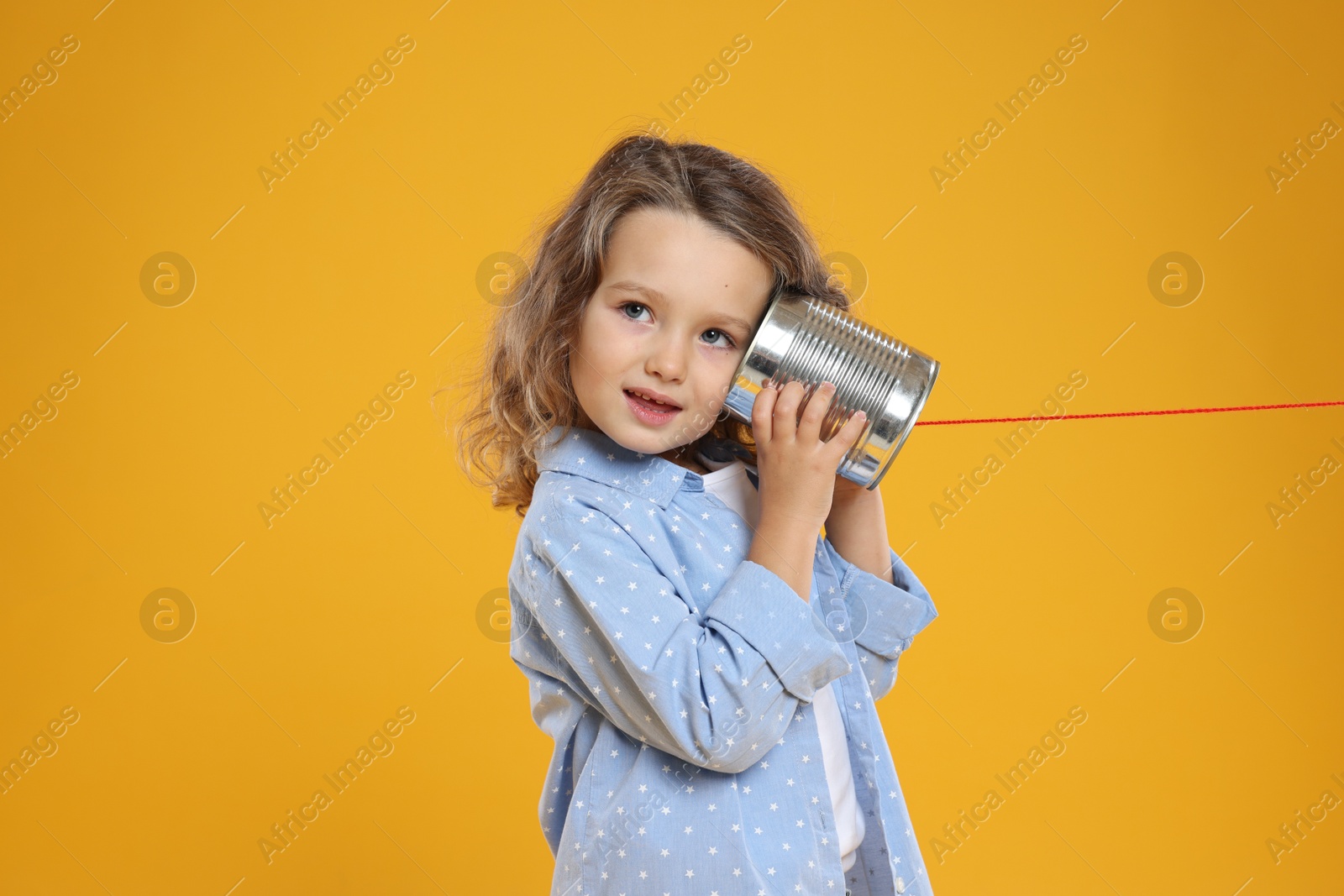 Photo of Girl using tin can telephone on orange background