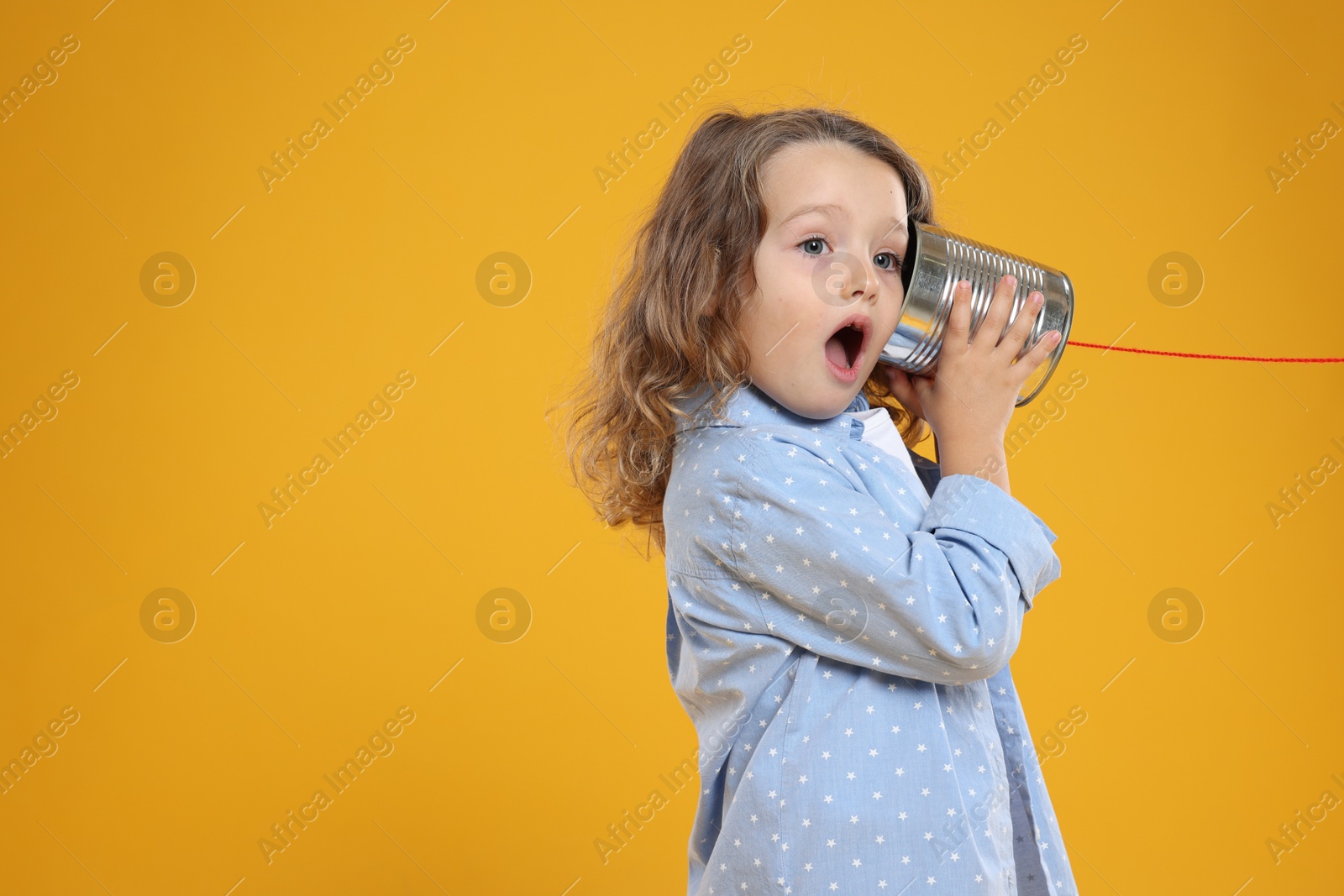 Photo of Emotional girl using tin can telephone on orange background. Space for text