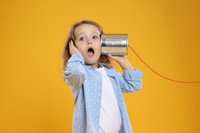 Photo of Emotional girl using tin can telephone on orange background