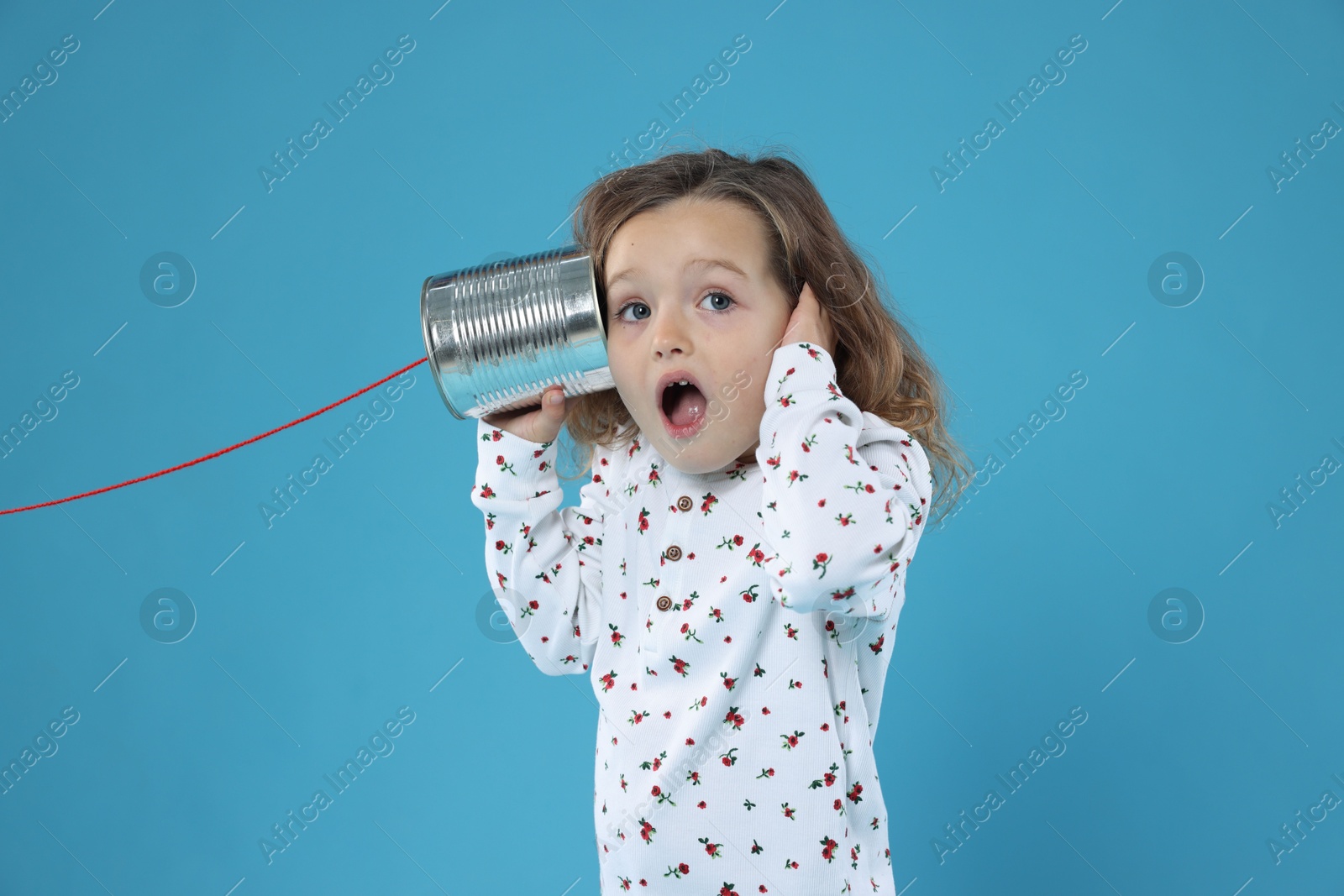 Photo of Surprised girl using tin can telephone on blue background