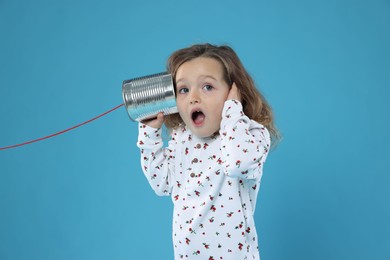 Photo of Surprised girl using tin can telephone on blue background