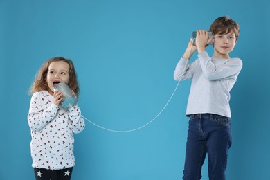 Photo of Boy and girl talking on tin can telephone against blue background