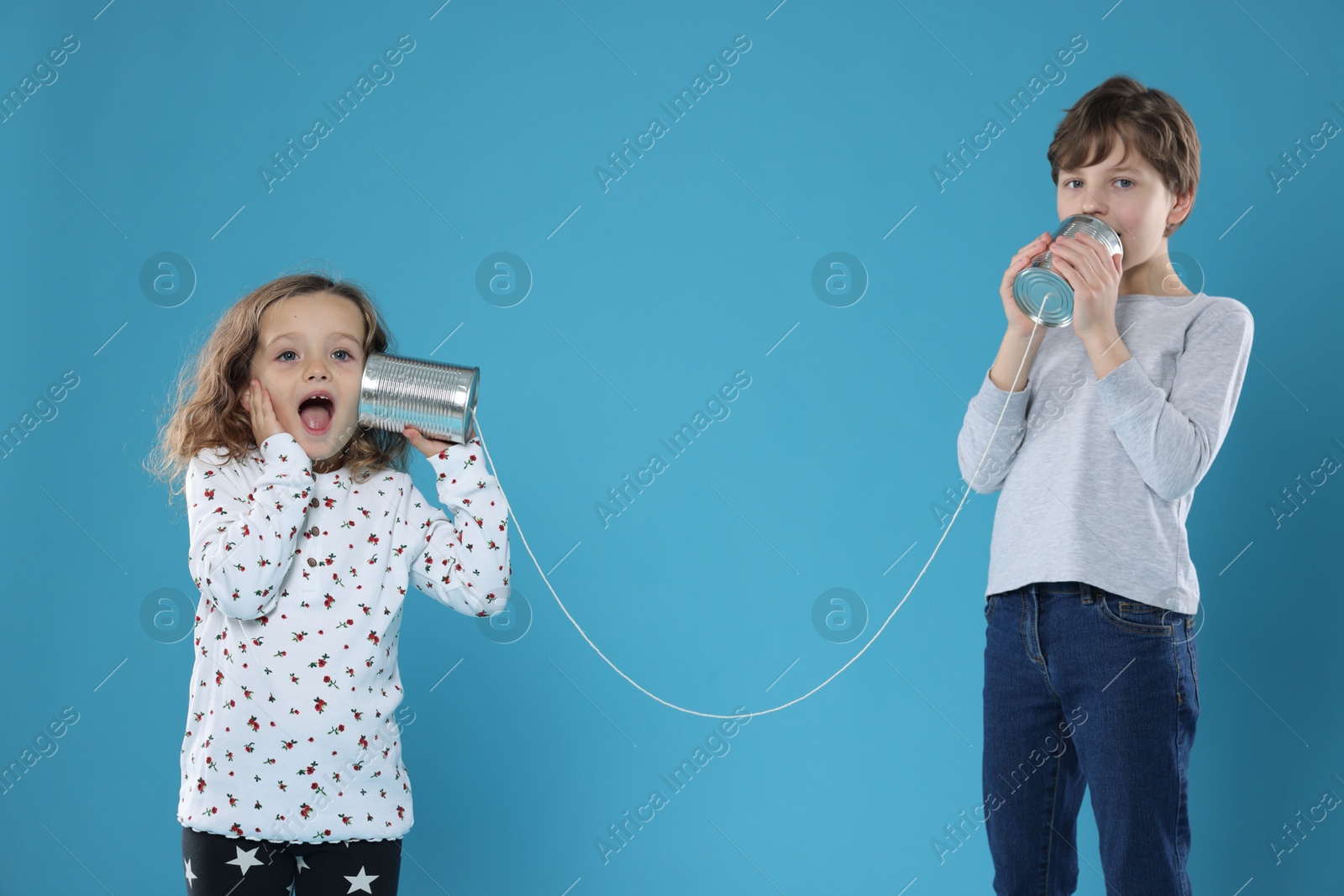 Photo of Boy and girl talking on tin can telephone against blue background